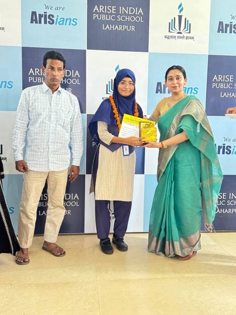 A student receiving a certificate of merit in front of the Arise India Public School branded backdrop